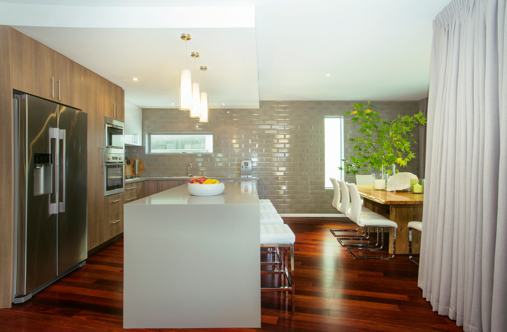 Modern inredning av ett mellanstort kök, med en dubbel diskho, bänkskiva i kvarts, grått stänkskydd, stänkskydd i keramik, rostfria vitvaror, mörkt trägolv, en köksö och rött golv