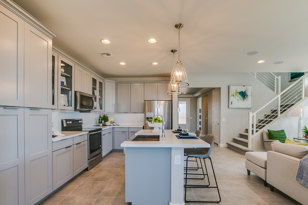 Inspiration for a large contemporary l-shaped ceramic tile and beige floor eat-in kitchen remodel in Phoenix with a drop-in sink, recessed-panel cabinets, gray cabinets, solid surface countertops, white backsplash, glass sheet backsplash, stainless steel appliances and an island