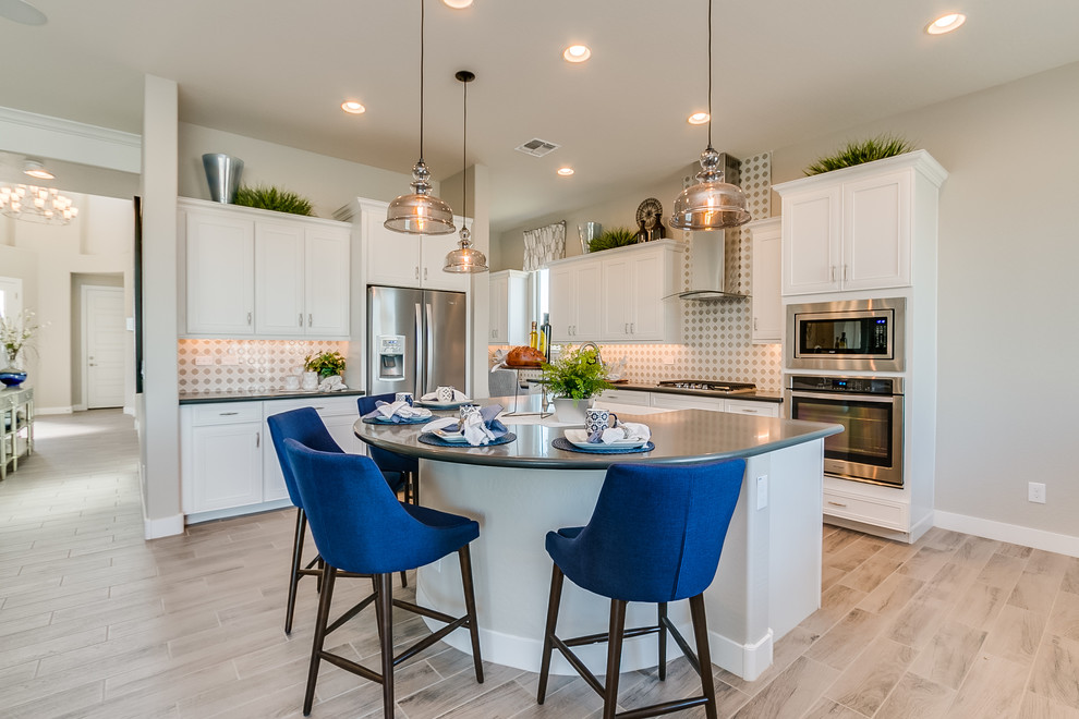 Example of a large trendy l-shaped ceramic tile and beige floor eat-in kitchen design in Phoenix with a farmhouse sink, recessed-panel cabinets, white cabinets, solid surface countertops, beige backsplash, ceramic backsplash, stainless steel appliances and an island