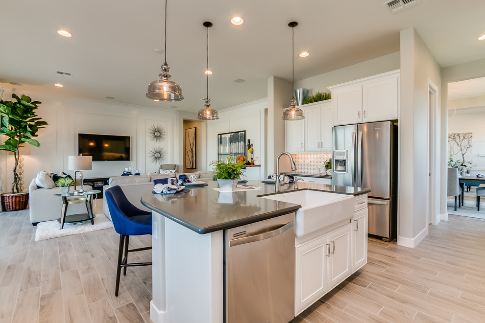 Photo of a large contemporary l-shaped kitchen/diner in Phoenix with a belfast sink, recessed-panel cabinets, white cabinets, composite countertops, beige splashback, ceramic splashback, stainless steel appliances, ceramic flooring, an island and beige floors.