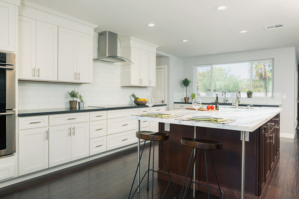 This is an example of a large contemporary u-shaped kitchen/diner in Atlanta with a submerged sink, shaker cabinets, white cabinets, granite worktops, white splashback, glass tiled splashback, stainless steel appliances, dark hardwood flooring and an island.