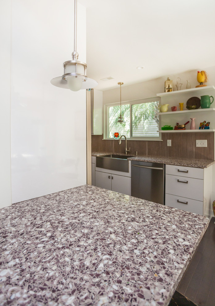 Modern inredning av ett stort kök, med en rustik diskho, vita skåp, rostfria vitvaror, släta luckor, bänkskiva i återvunnet glas, brunt stänkskydd, stänkskydd i cementkakel och klinkergolv i porslin