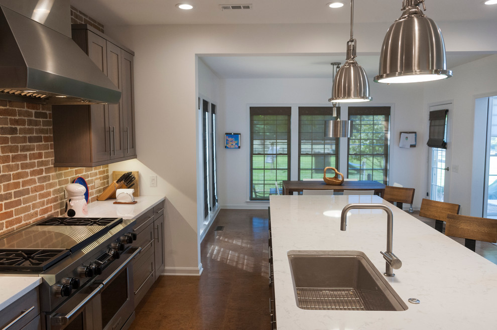 Foto på ett stort kök, med bänkskiva i kvarts, rostfria vitvaror, korkgolv, en köksö, en undermonterad diskho, grå skåp, stänkskydd i tegel och brunt golv