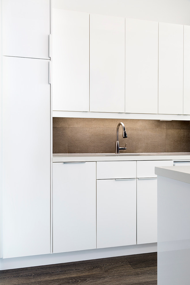 Industrial single-wall open plan kitchen in Toronto with a single-bowl sink, flat-panel cabinets, white cabinets, composite countertops, grey splashback, stone tiled splashback, white appliances, dark hardwood flooring and an island.