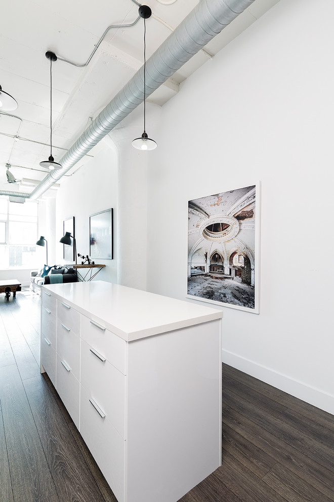 Industrial single-wall open plan kitchen in Toronto with a single-bowl sink, flat-panel cabinets, white cabinets, engineered stone countertops, grey splashback, stone tiled splashback, white appliances, dark hardwood flooring and an island.