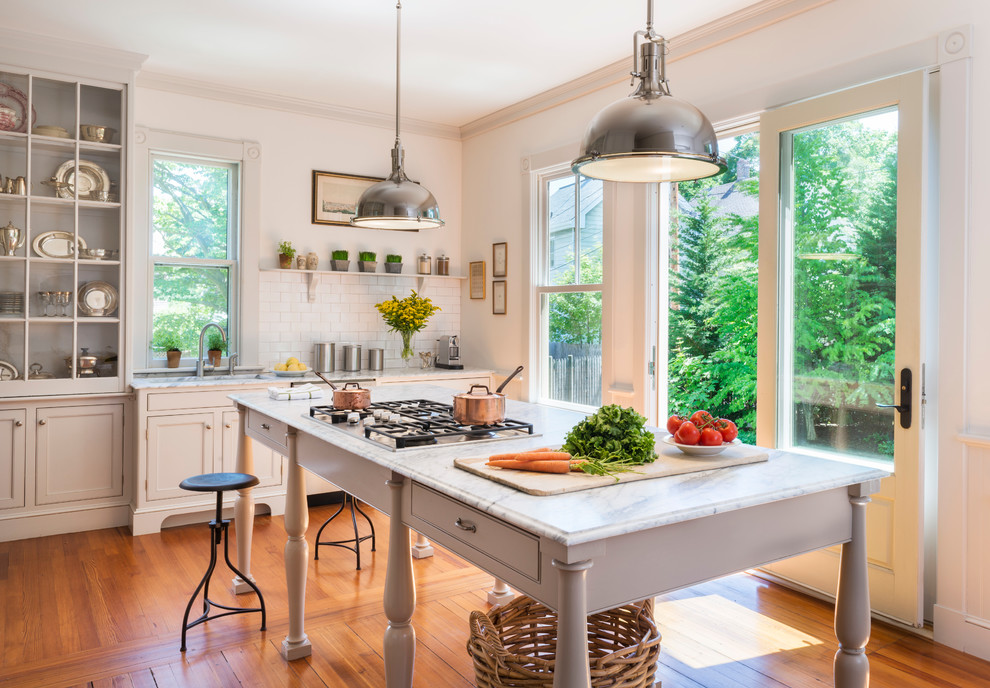 Bild på ett stort lantligt kök med öppen planlösning, med en undermonterad diskho, luckor med infälld panel, grå skåp, marmorbänkskiva, vitt stänkskydd, stänkskydd i tunnelbanekakel, mellanmörkt trägolv, en köksö och brunt golv
