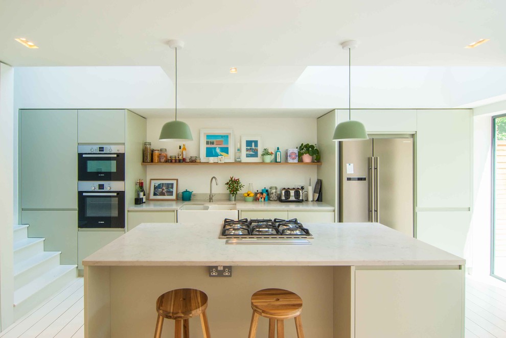 Design ideas for a medium sized modern single-wall kitchen in London with a double-bowl sink, flat-panel cabinets, green cabinets, granite worktops, stainless steel appliances, painted wood flooring, an island and white floors.