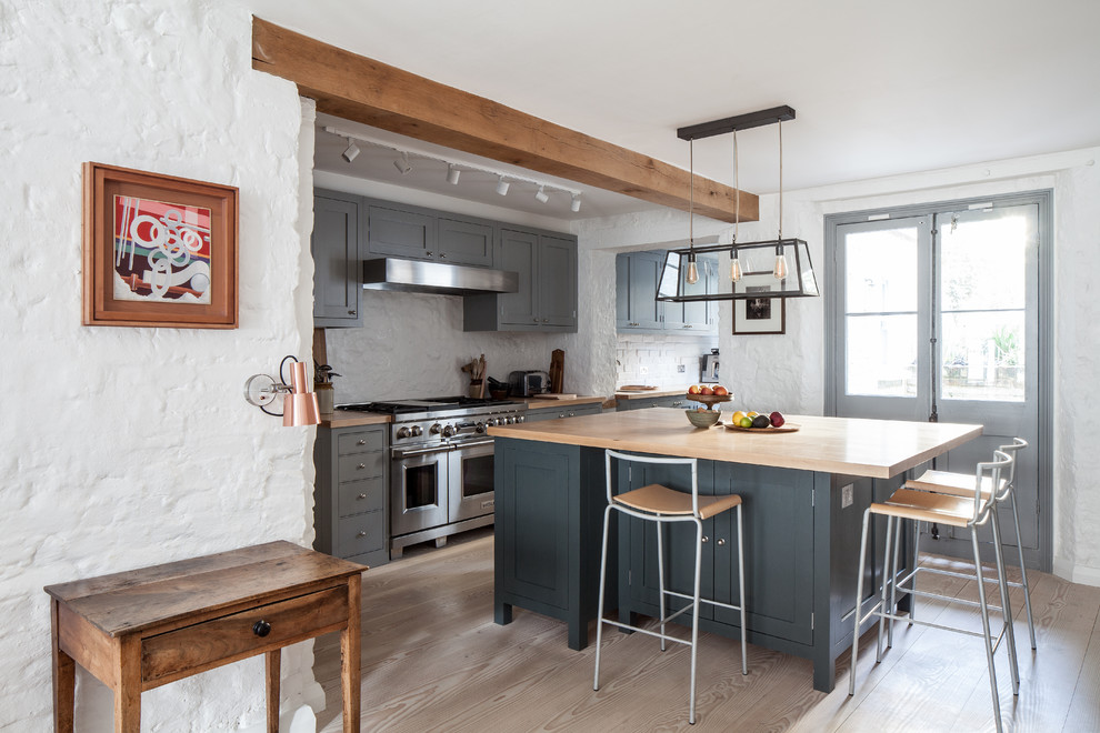 Bild på ett lantligt beige beige kök, med luckor med profilerade fronter, grå skåp, träbänkskiva, rostfria vitvaror, ljust trägolv, en köksö och beiget golv