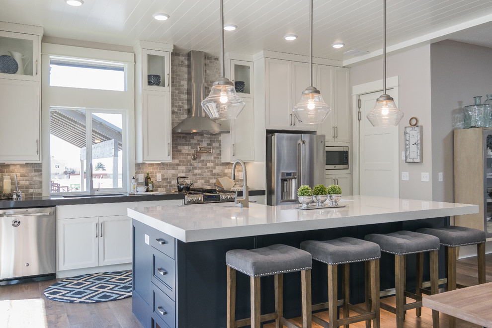Transitional galley medium tone wood floor open concept kitchen photo in Salt Lake City with recessed-panel cabinets, blue cabinets, gray backsplash, stainless steel appliances and an island