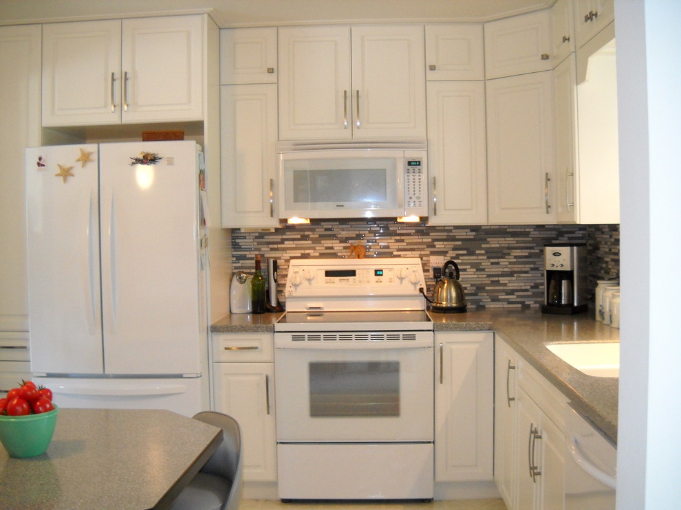 Kleine Moderne Wohnküche ohne Insel in L-Form mit Unterbauwaschbecken, profilierten Schrankfronten, weißen Schränken, Mineralwerkstoff-Arbeitsplatte, Küchenrückwand in Grau, Rückwand aus Stäbchenfliesen, weißen Elektrogeräten und Linoleum in Vancouver