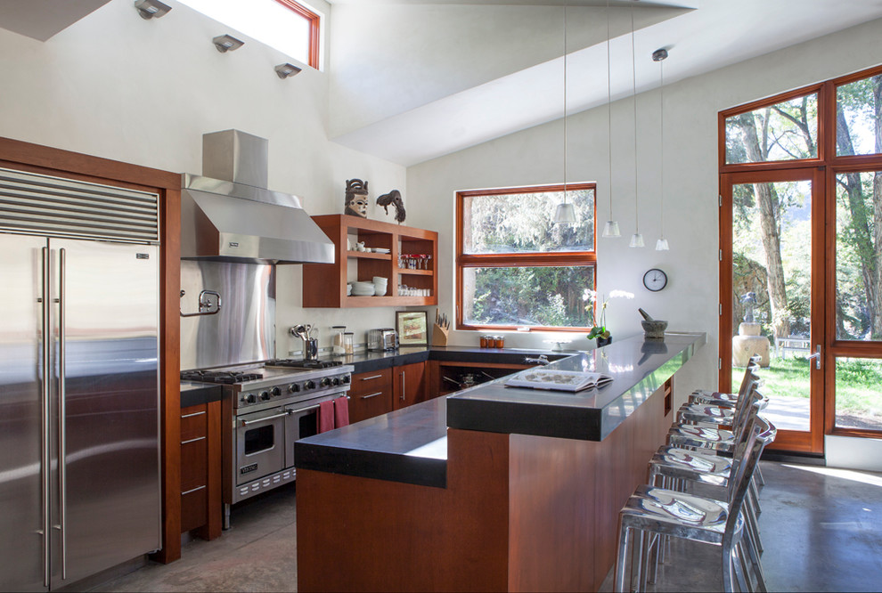 Moderne Küche mit hellbraunen Holzschränken, Küchenrückwand in Metallic, Küchengeräten aus Edelstahl, Betonboden und Halbinsel in Denver