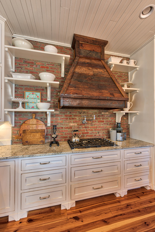 Kitchen - mid-sized country l-shaped medium tone wood floor kitchen idea in Other with a farmhouse sink, flat-panel cabinets, white cabinets, quartzite countertops, multicolored backsplash, brick backsplash, stainless steel appliances and an island