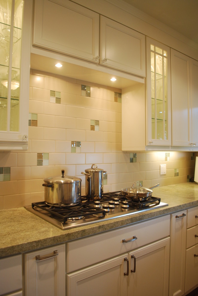 Example of a mid-sized classic u-shaped medium tone wood floor and brown floor enclosed kitchen design in San Francisco with recessed-panel cabinets, white cabinets, granite countertops, multicolored backsplash, porcelain backsplash, paneled appliances and an island