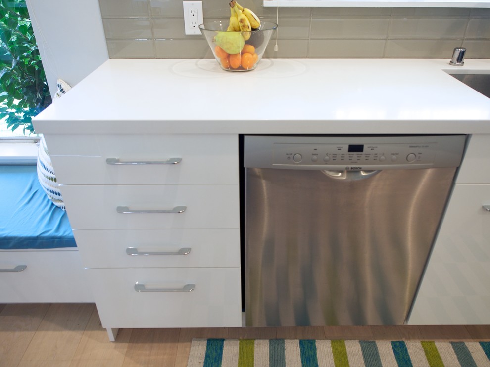 Example of a mid-sized trendy l-shaped medium tone wood floor enclosed kitchen design in San Francisco with an undermount sink, flat-panel cabinets, white cabinets, quartz countertops, gray backsplash, glass tile backsplash, stainless steel appliances and an island