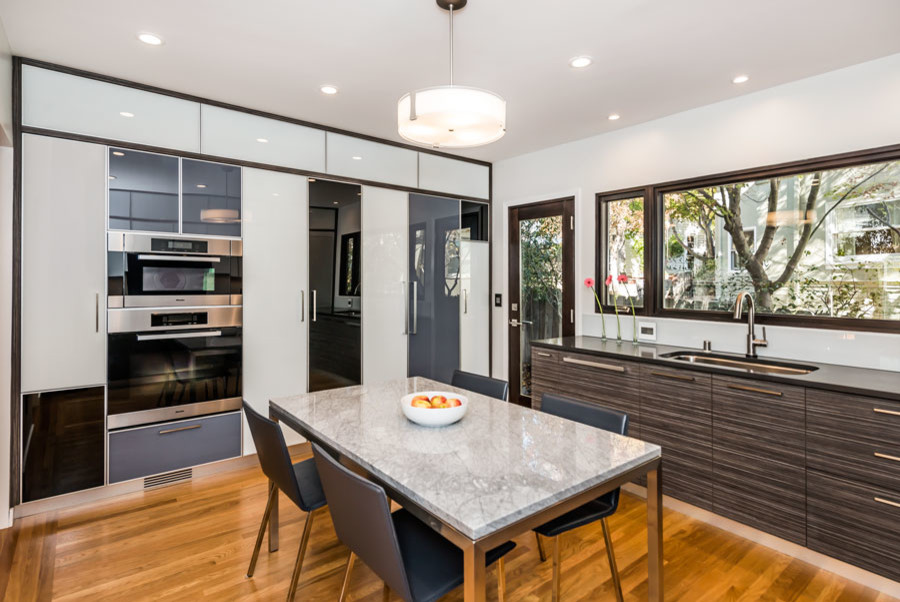 Inspiration for a mid-sized modern u-shaped light wood floor eat-in kitchen remodel in San Francisco with a single-bowl sink, glass-front cabinets, quartz countertops, glass sheet backsplash, stainless steel appliances, black backsplash and no island
