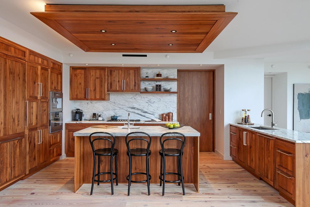 Inspiration for a transitional u-shaped light wood floor and beige floor kitchen remodel in New York with an undermount sink, shaker cabinets, medium tone wood cabinets, gray backsplash, an island, gray countertops and stone slab backsplash