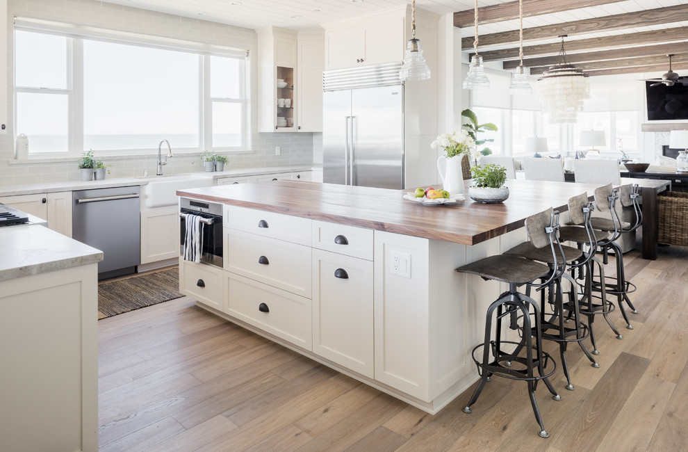 Example of a mid-sized beach style u-shaped eat-in kitchen design in Los Angeles with shaker cabinets, white cabinets, solid surface countertops and an island