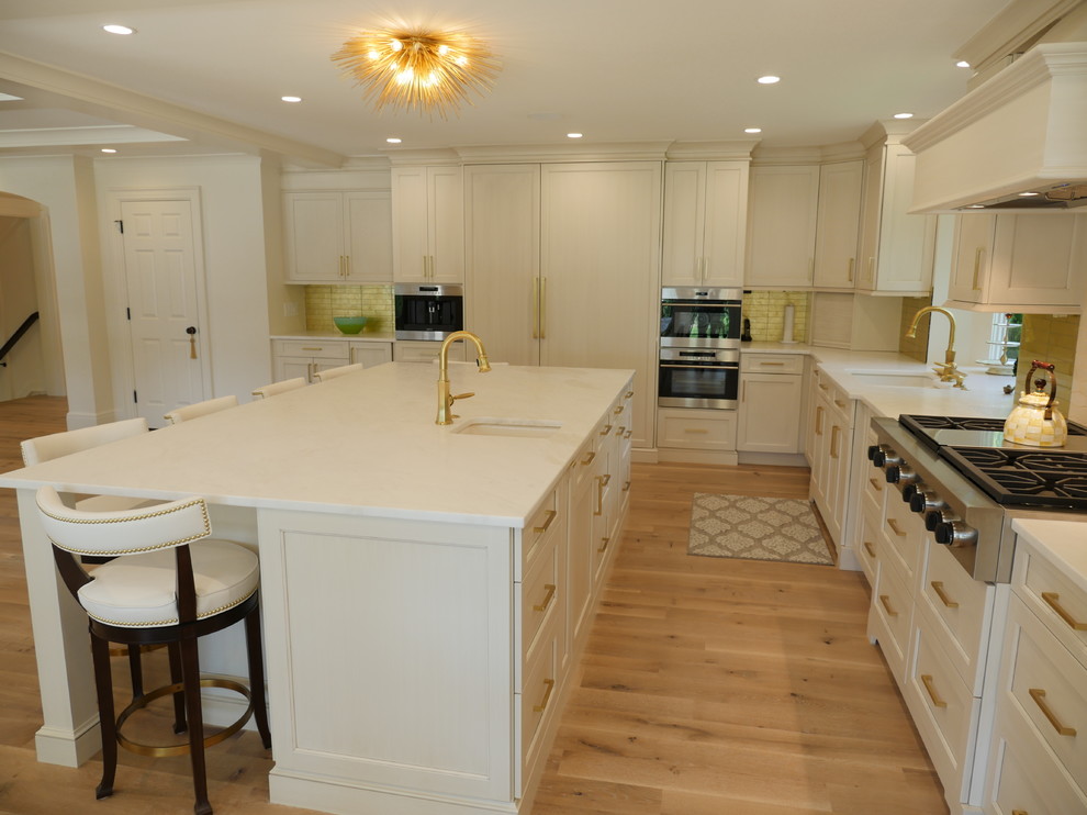 Large traditional l-shaped kitchen/diner in Detroit with recessed-panel cabinets, beige cabinets, light hardwood flooring, an island, a submerged sink, engineered stone countertops, yellow splashback, glass tiled splashback and stainless steel appliances.
