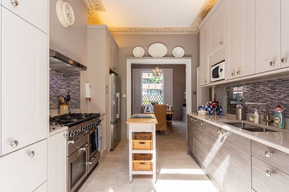 ロンドンにある中くらいなトランジショナルスタイルのおしゃれなキッチン (ダブルシンク、フラットパネル扉のキャビネット、グレーのキッチンパネル、シルバーの調理設備、グレーの床、白いキッチンカウンター) の写真