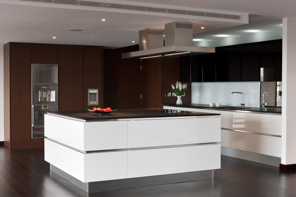 This is an example of a large contemporary l-shaped open plan kitchen in London with white cabinets, an island, flat-panel cabinets, engineered stone countertops, metallic splashback and mirror splashback.