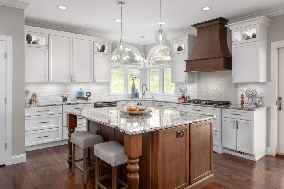 Inspiration for a large transitional l-shaped medium tone wood floor and brown floor eat-in kitchen remodel in St Louis with an undermount sink, white cabinets, granite countertops, ceramic backsplash, stainless steel appliances, an island, shaker cabinets, white backsplash and gray countertops