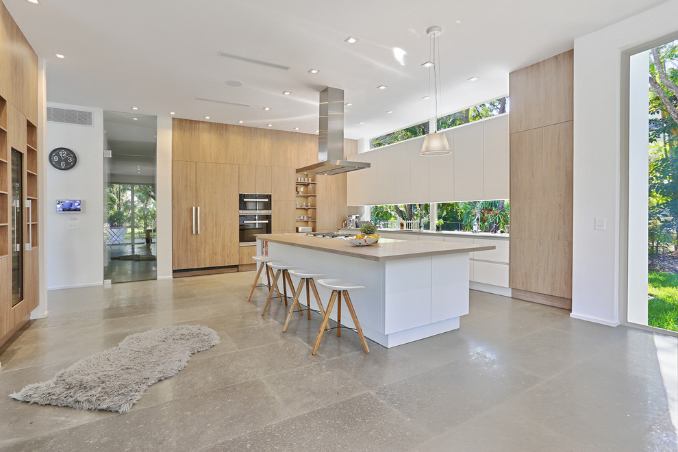 Foto på ett stort funkis kök, med en undermonterad diskho, släta luckor, vita skåp, bänkskiva i betong, fönster som stänkskydd, integrerade vitvaror, betonggolv och en köksö