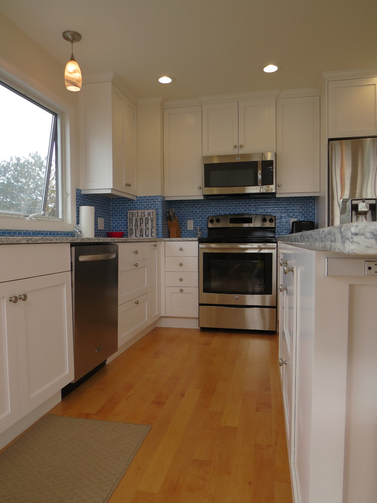 Exempel på ett mellanstort maritimt kök, med en undermonterad diskho, skåp i shakerstil, vita skåp, bänkskiva i kvarts, blått stänkskydd, stänkskydd i glaskakel, rostfria vitvaror, ljust trägolv och en köksö
