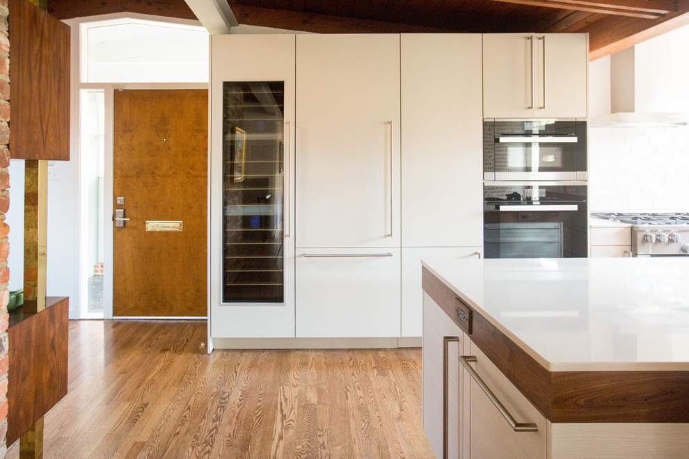 Inspiration for a mid-sized 1960s l-shaped medium tone wood floor, brown floor and wood ceiling eat-in kitchen remodel in DC Metro with an undermount sink, flat-panel cabinets, white cabinets, white backsplash, paneled appliances, an island, white countertops, quartz countertops and ceramic backsplash