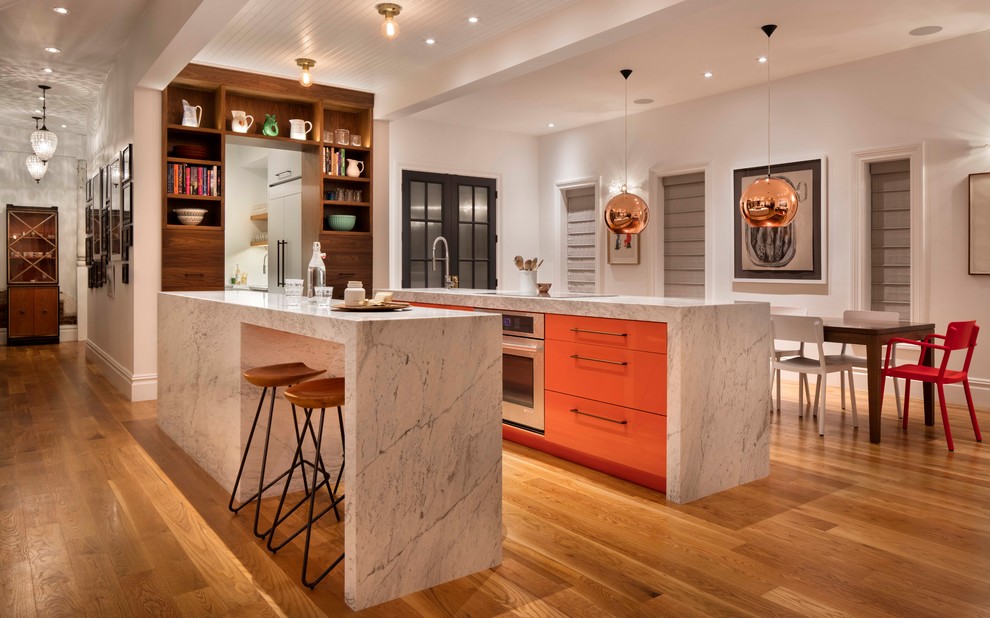 Zweizeilige Moderne Wohnküche mit Unterbauwaschbecken, flächenbündigen Schrankfronten, orangefarbenen Schränken, Küchengeräten aus Edelstahl, braunem Holzboden, zwei Kücheninseln, braunem Boden und weißer Arbeitsplatte in Denver