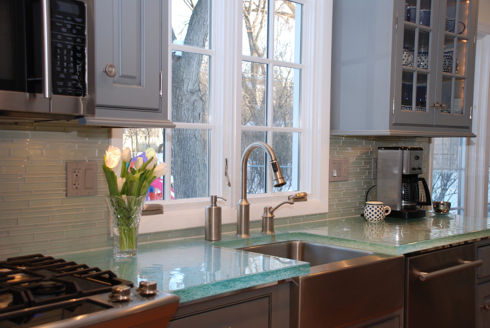 Inredning av ett modernt mellanstort kök, med en rustik diskho, luckor med profilerade fronter, grå skåp, bänkskiva i glas, grått stänkskydd, stänkskydd i tunnelbanekakel, rostfria vitvaror och mellanmörkt trägolv