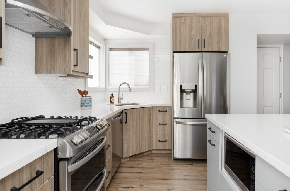 Klassisk inredning av ett mellanstort vit vitt kök, med en undermonterad diskho, släta luckor, skåp i ljust trä, bänkskiva i kvarts, vitt stänkskydd, stänkskydd i stenkakel, rostfria vitvaror, laminatgolv, en köksö och brunt golv