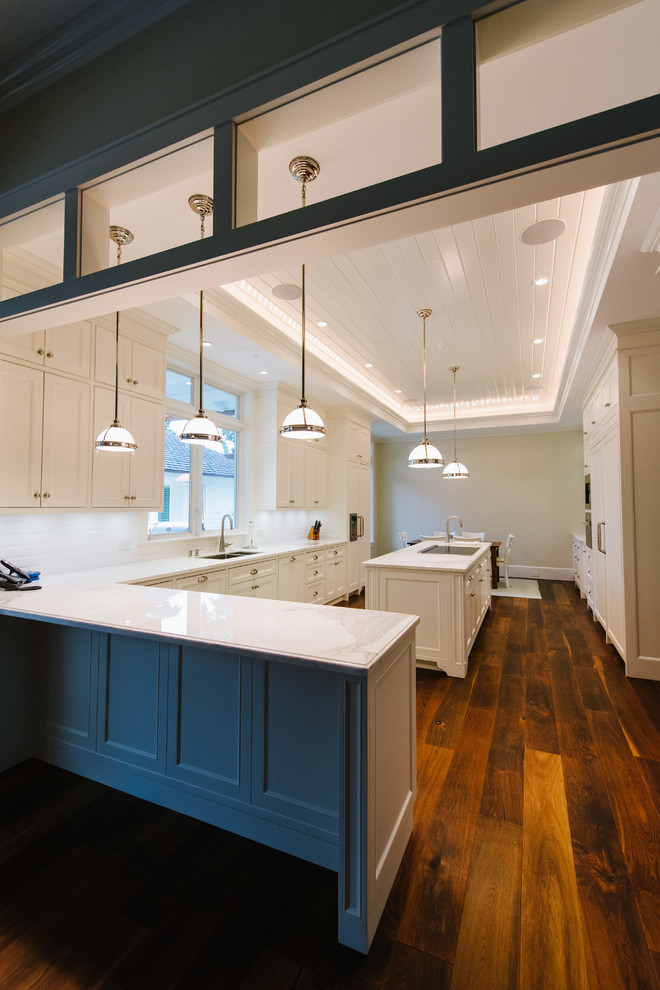 Inspiration for a mid-sized transitional l-shaped medium tone wood floor and beige floor enclosed kitchen remodel in Miami with a double-bowl sink, shaker cabinets, white cabinets, quartz countertops, white backsplash, ceramic backsplash, paneled appliances and an island