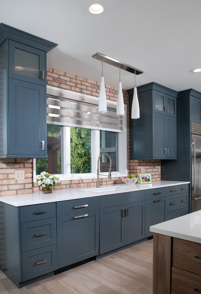 Eat-in kitchen - mid-sized traditional l-shaped light wood floor eat-in kitchen idea in Grand Rapids with an undermount sink, recessed-panel cabinets, blue cabinets, quartzite countertops, multicolored backsplash, brick backsplash, stainless steel appliances and an island
