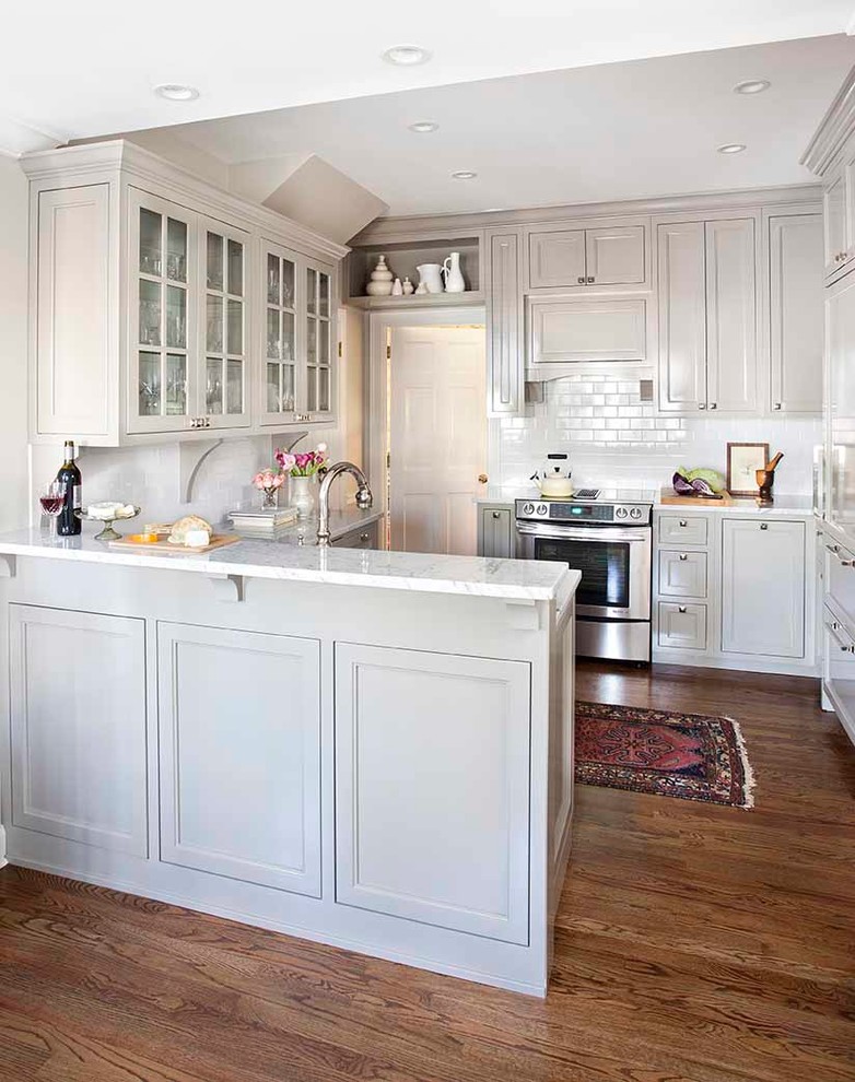 Foto på ett litet vintage u-kök, med en rustik diskho, luckor med infälld panel, grå skåp, marmorbänkskiva, vitt stänkskydd, stänkskydd i tunnelbanekakel, integrerade vitvaror och mellanmörkt trägolv