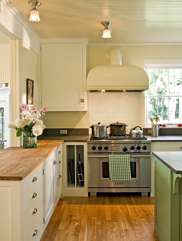Example of a classic kitchen design in Portland Maine with wood countertops, shaker cabinets, white cabinets, white backsplash, subway tile backsplash and stainless steel appliances
