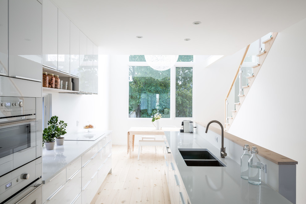 Zweizeilige, Mittelgroße Moderne Wohnküche mit Doppelwaschbecken, flächenbündigen Schrankfronten, weißen Schränken, hellem Holzboden und Kücheninsel in Ottawa