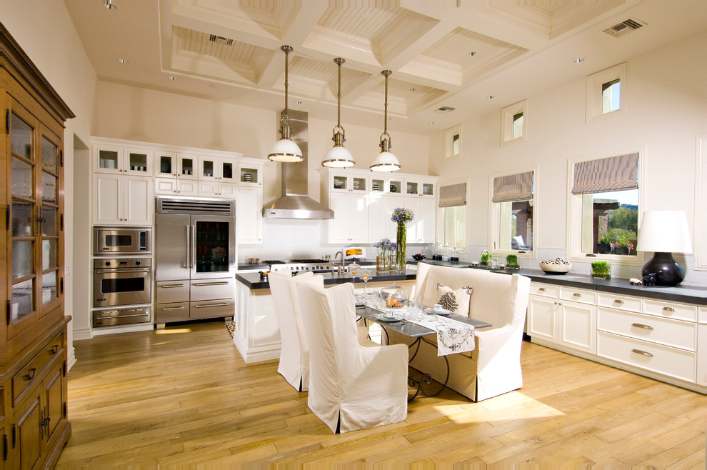 Imagen de cocina comedor mediterránea con electrodomésticos de acero inoxidable, armarios con paneles empotrados, puertas de armario blancas, salpicadero blanco y cortinas