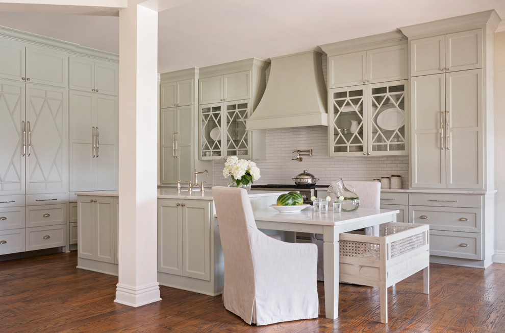 Diseño de cocina tradicional con puertas de armario grises, salpicadero blanco, suelo de madera en tonos medios, una isla, encimeras blancas, armarios con paneles empotrados y barras de cocina