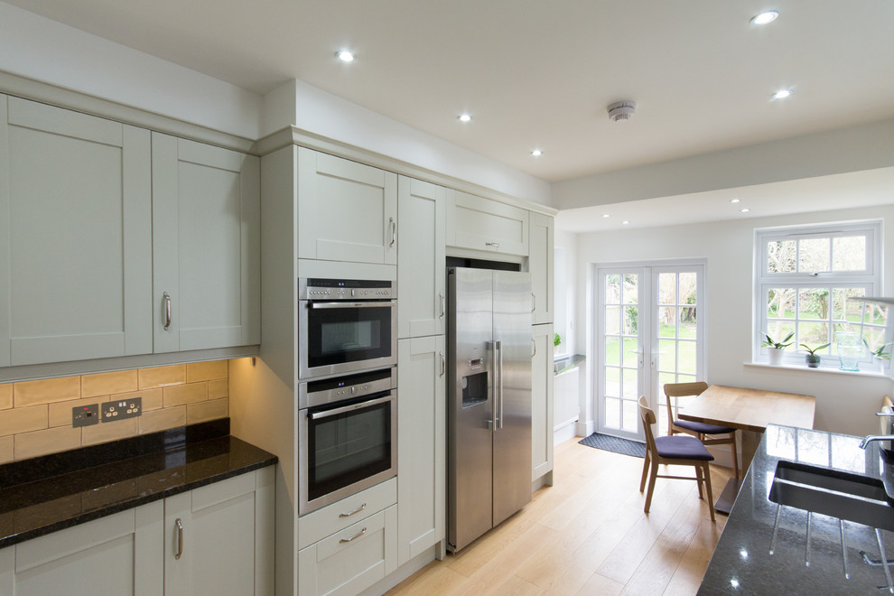Medium sized contemporary l-shaped kitchen/diner in London with an integrated sink, shaker cabinets, green cabinets, granite worktops, green splashback, porcelain splashback, stainless steel appliances, medium hardwood flooring and no island.