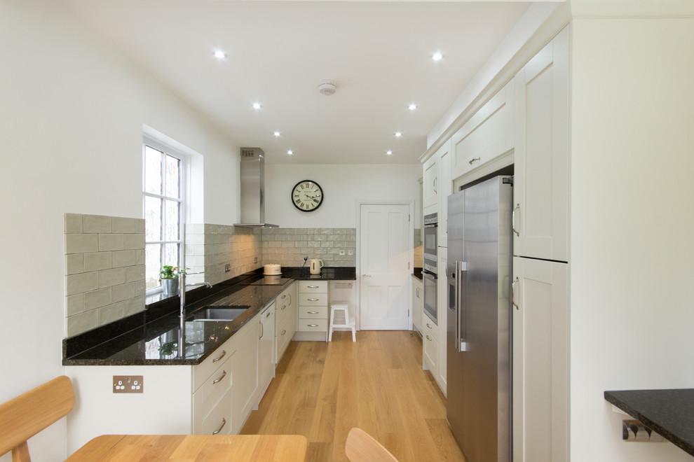 Design ideas for a medium sized contemporary galley kitchen/diner in London with a built-in sink, shaker cabinets, granite worktops, green splashback, porcelain splashback, stainless steel appliances, medium hardwood flooring, no island and green cabinets.