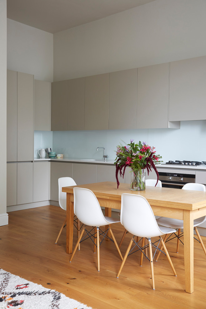 This is an example of a medium sized contemporary l-shaped kitchen/diner in London with flat-panel cabinets, beige cabinets, quartz worktops, blue splashback, glass tiled splashback, medium hardwood flooring, no island and white worktops.