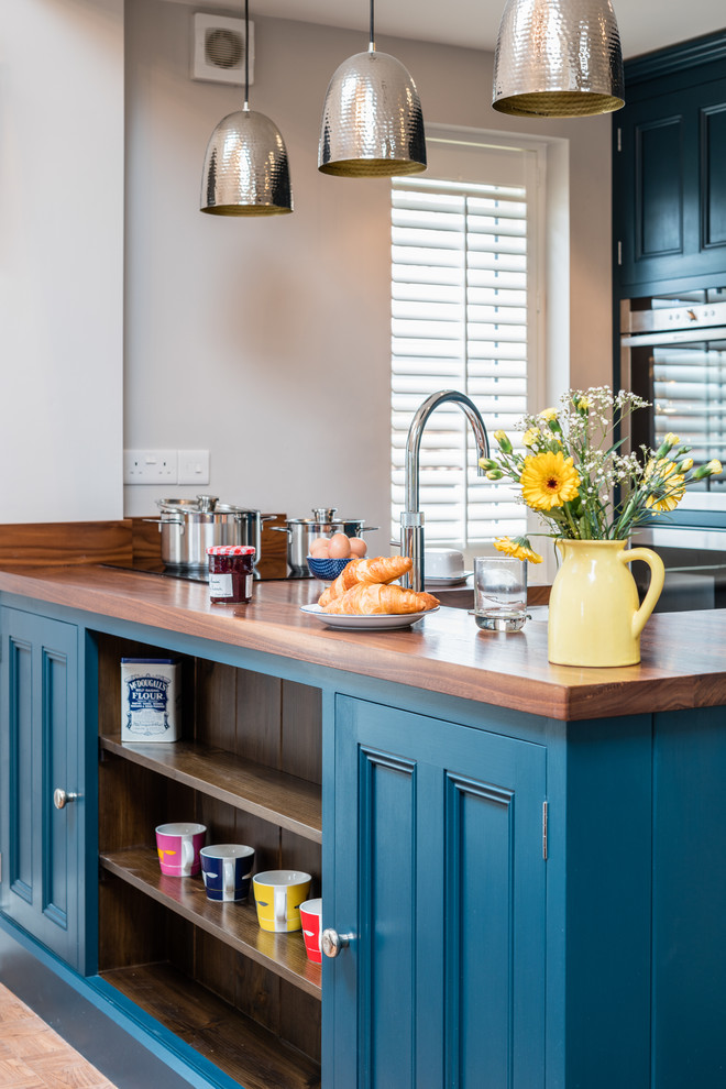 Cette image montre une petite cuisine ouverte rustique avec un placard avec porte à panneau encastré, des portes de placard bleues, un plan de travail en bois, un électroménager en acier inoxydable et une péninsule.