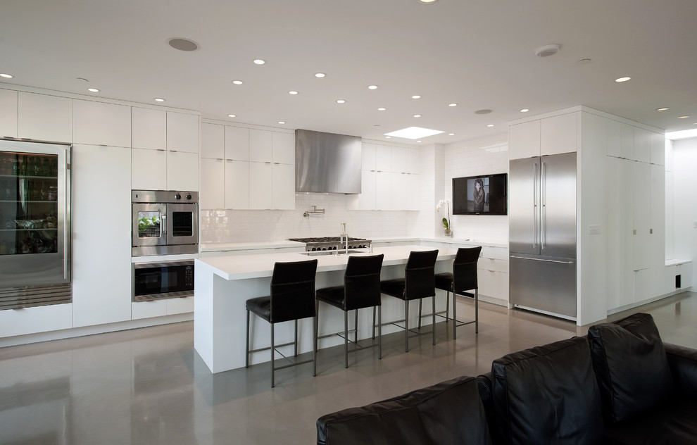 Inspiration for a modern l-shaped concrete floor open concept kitchen remodel in Seattle with stainless steel appliances, flat-panel cabinets, white cabinets, solid surface countertops, white backsplash, ceramic backsplash and an island