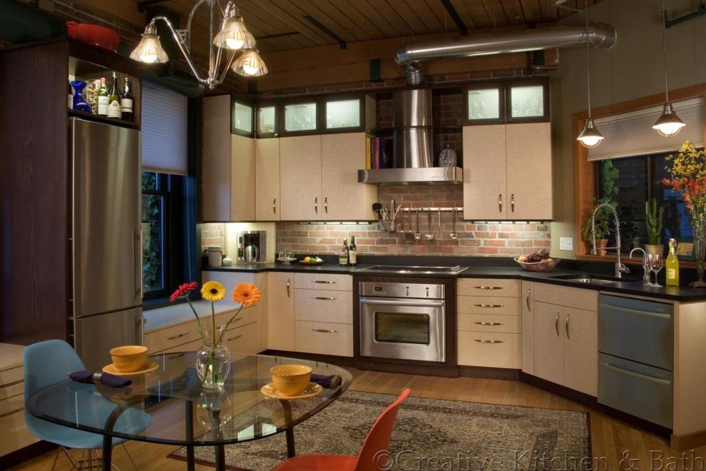 Eat-in kitchen - mid-sized eclectic medium tone wood floor eat-in kitchen idea in Seattle with a single-bowl sink, flat-panel cabinets, light wood cabinets, solid surface countertops, brick backsplash, stainless steel appliances and no island