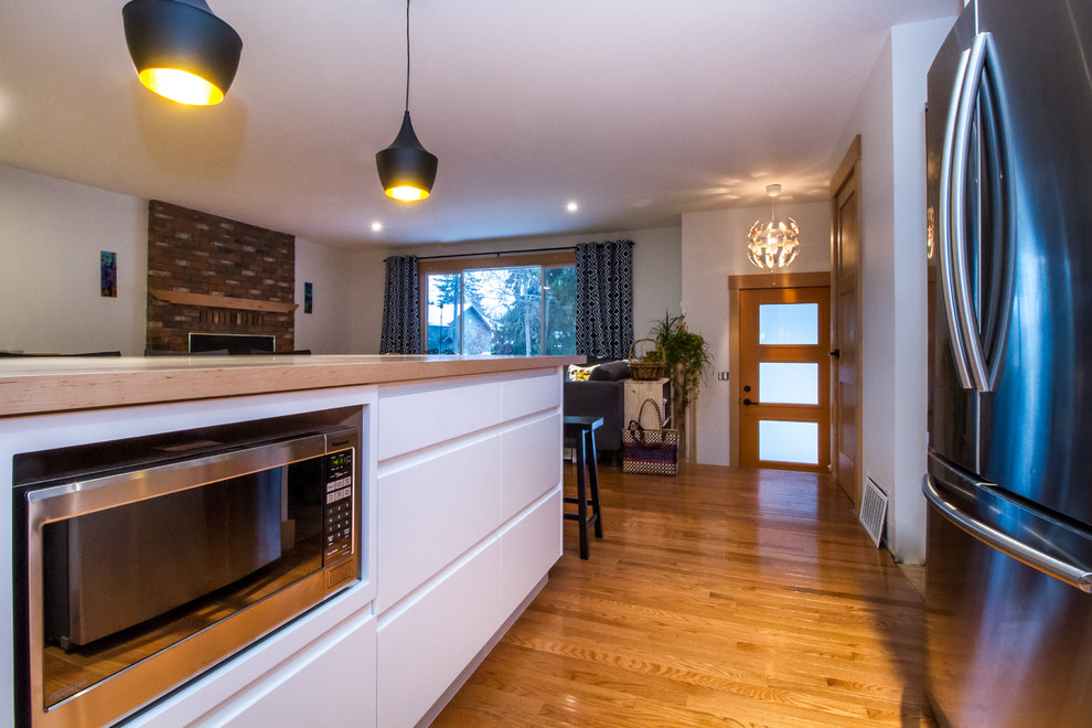 Modern inredning av ett mellanstort kök, med släta luckor, vita skåp, träbänkskiva, stänkskydd i keramik, rostfria vitvaror, ljust trägolv och en köksö