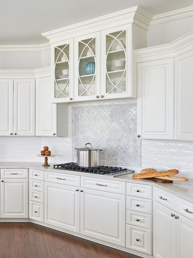Inredning av ett klassiskt stort vit vitt kök, med en undermonterad diskho, luckor med upphöjd panel, vita skåp, marmorbänkskiva, vitt stänkskydd, stänkskydd i keramik, integrerade vitvaror, mörkt trägolv, en köksö och brunt golv