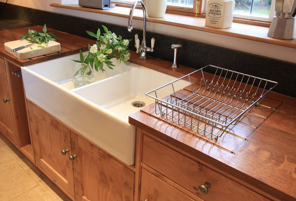 This is an example of a medium sized rural kitchen in London with a belfast sink, beaded cabinets, medium wood cabinets, wood worktops, stainless steel appliances and limestone flooring.