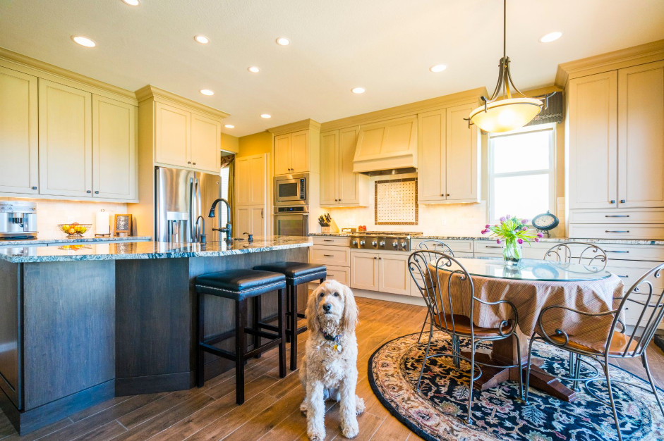 Example of a large classic l-shaped brown floor and medium tone wood floor eat-in kitchen design in Denver with a farmhouse sink, recessed-panel cabinets, granite countertops, porcelain backsplash, stainless steel appliances, an island, beige cabinets and beige backsplash