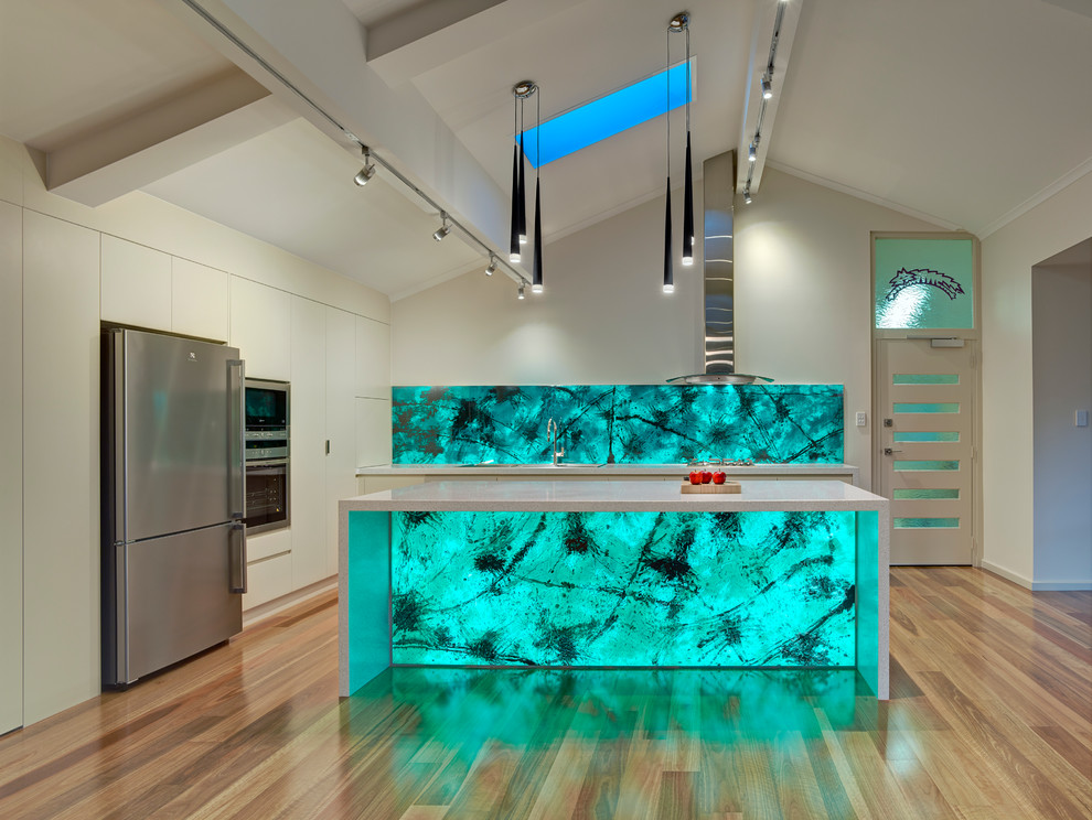 Идея дизайна: огромная кухня-гостиная в современном стиле с накладной мойкой, зеленым фартуком, фартуком из стеклянной плитки, техникой из нержавеющей стали, светлым паркетным полом и островом