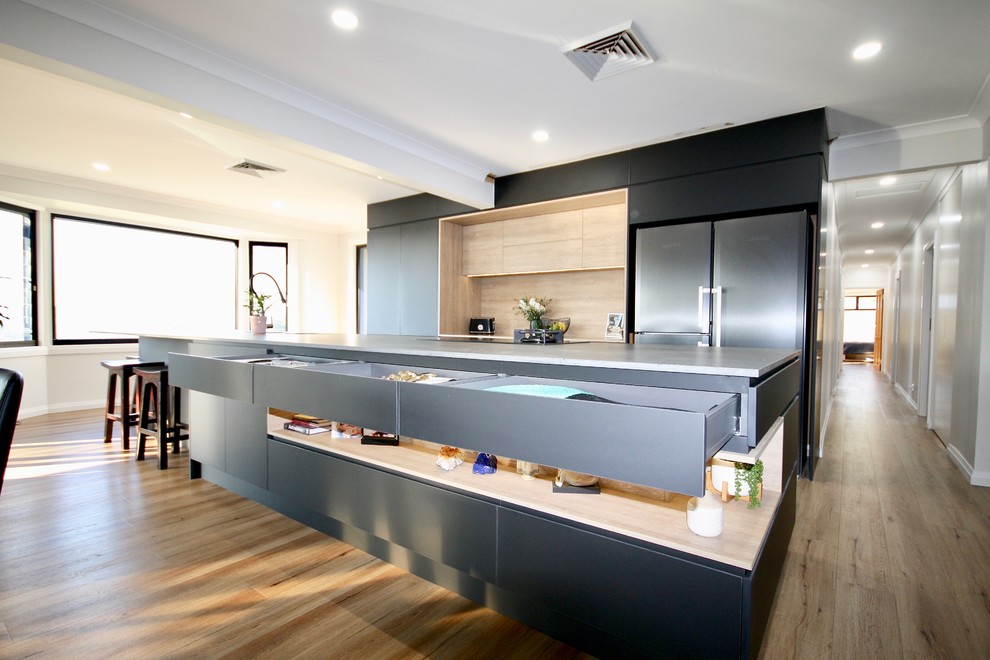 Photo of a large modern single-wall kitchen/diner in Sydney with a submerged sink, flat-panel cabinets, black cabinets, engineered stone countertops, black appliances, medium hardwood flooring, an island, brown floors and grey worktops.